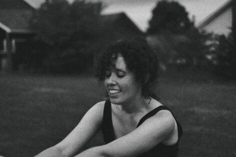 Black and white image of a white person with dark curly hair. She is looking down and smiling. Photo by Steve Dillon.