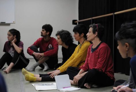 Barbara Mahler teaching in Chile in 2018. A group of students are seated next to her in a semi circle, they are looking at the space in front of them, their sides of the bodies facing the camera. Photo courtesy of the artist.