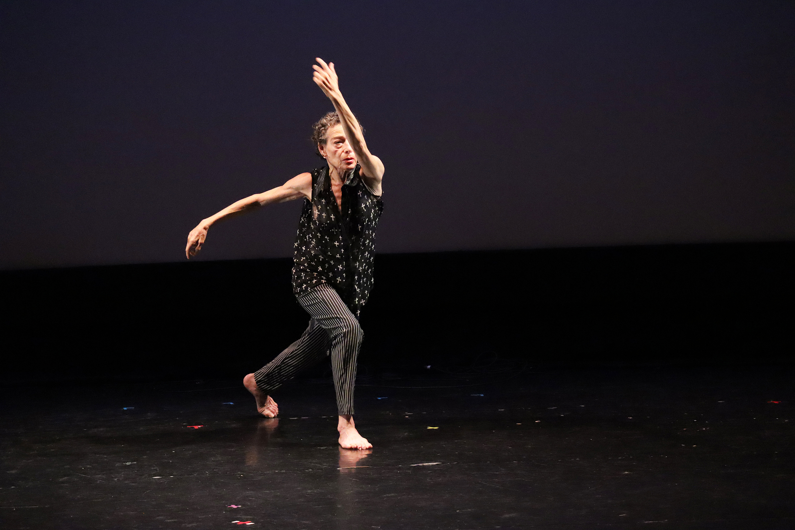 Photo of Barbara performing on stage. She is lunging forward, one arm is extending sideways and the other is extending upwards diagonally. Photo courtesy of the artist.