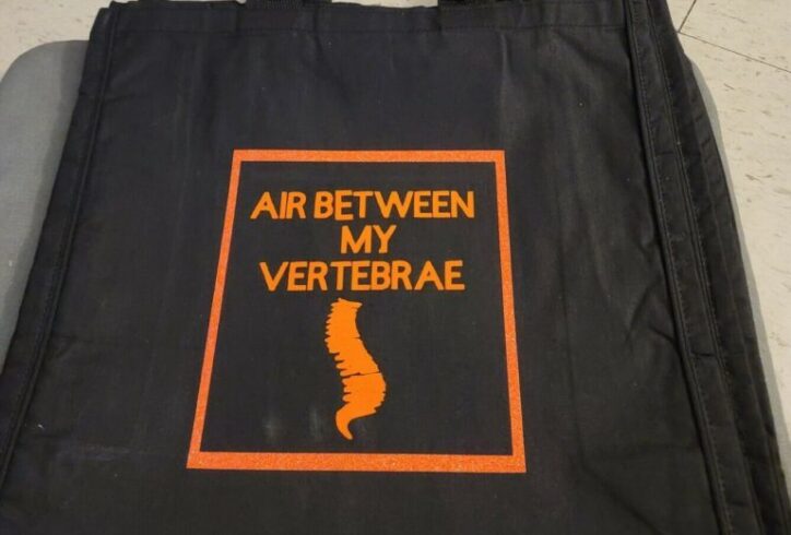 Photo of a black canvas bag with the words Air Between by Vertebrae written in orange and a small image of a spine printed on it. Photo courtesy of Dark Room Ballet