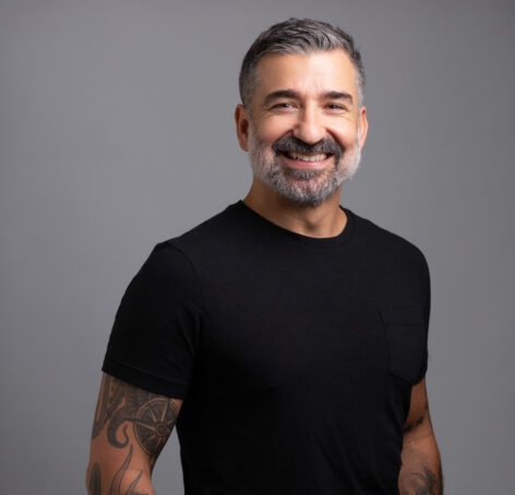 Photo of Fabio Tavares posing in a studio. He is wearing a black t-shirt and smiling into the camera.