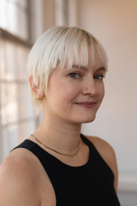 Portrait of Amanda. She has short platinum blonde hair and is wearing a black tank top. She looks at the camera with a neutral expression.