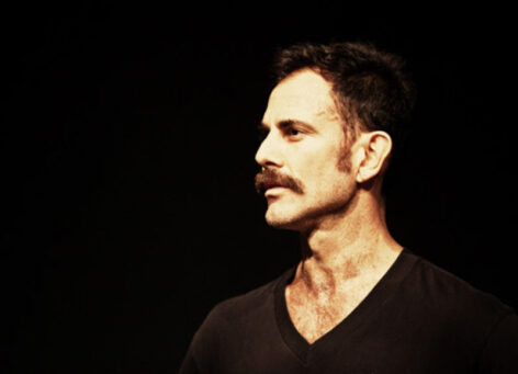 A portrait shot of Wally. He wears a black shirt in front of a dark background. He is a white male with a brown mustache and brown hair.