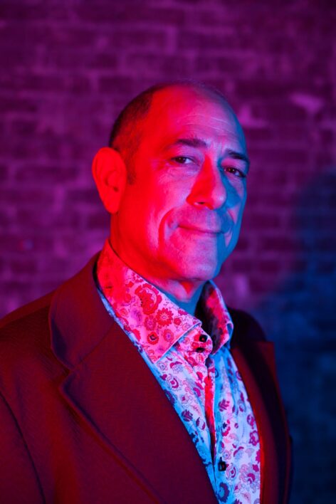close up of a white middle aged man in a vintage maroon blazer. Photo by Aundre Larrow