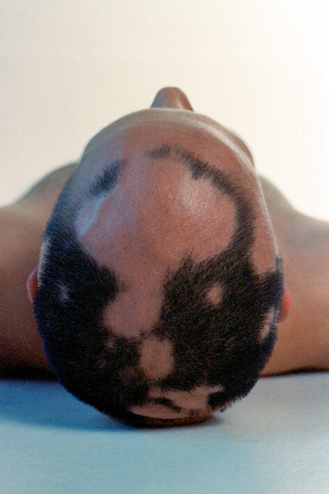 A picture of Demetris lying down, with their head tilted backward against a neutral background. Photo by Hudson Bohr