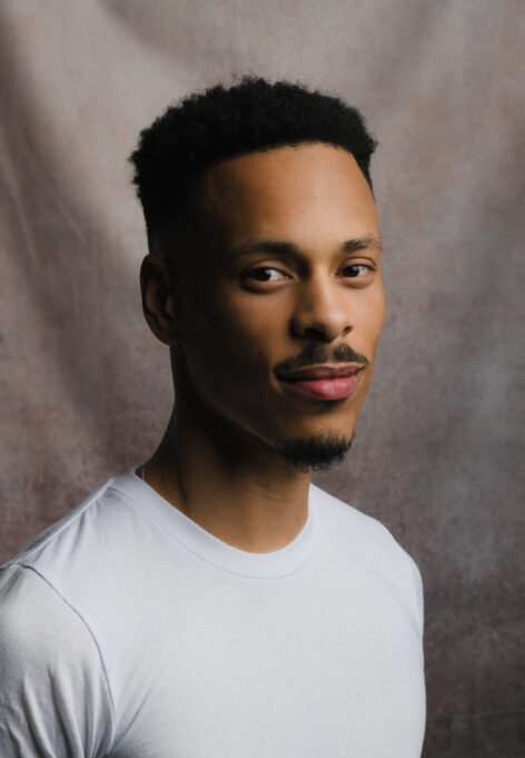 black male in white tshirt looking forward with a gray back drop. Photo by Emily Farthing.