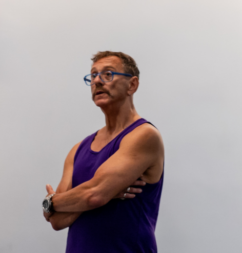 Neil a white cis-man with short brown hair and brown moustache. Neil teaching for Summer MELT 2025 in a purple tank top and glasses. Photo by Rachel Keane.