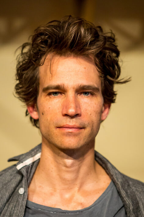 A man with brown hair in a grey shirt looking directly towards the camera. Photo by Peter Raper.