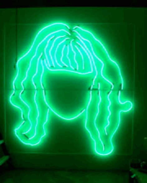 A neon green sign of a face with wavy hair and bangs. Photo by Paula Court.