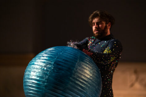 A dancer in a rhinestoned sapphire bodysuit holds a paper globe in Judson Church. photo by Rachel Keane.