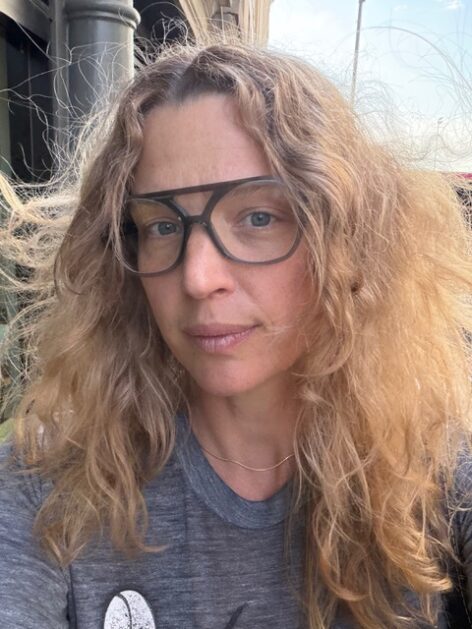 Rebecca Brooks looks in to the camera with brown framed glasses. Photo courtesy of the artist.