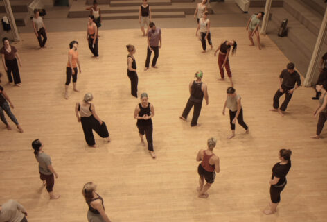 A group of dancers walks through St. Marks Church during a class. The photo is taken from above. The floor is a blonde wood. Photo by Tori Lawrence.