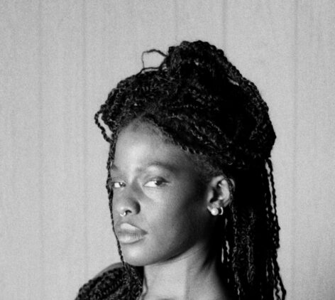 Black and grey photo of Morgan. She looks to the camera in a three quarter pose from the neck up. Her hair in braids sits half up and half down. Photo courtesy of the artist.