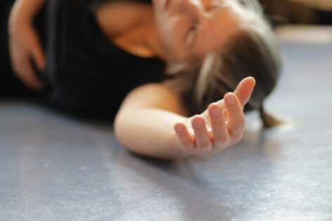 Photo of a person laying on a studio floor. Their head is almost touching the floor. Their arm reaches towards the camera and the fingers are relaxed. Photo by Otto Ramstad.