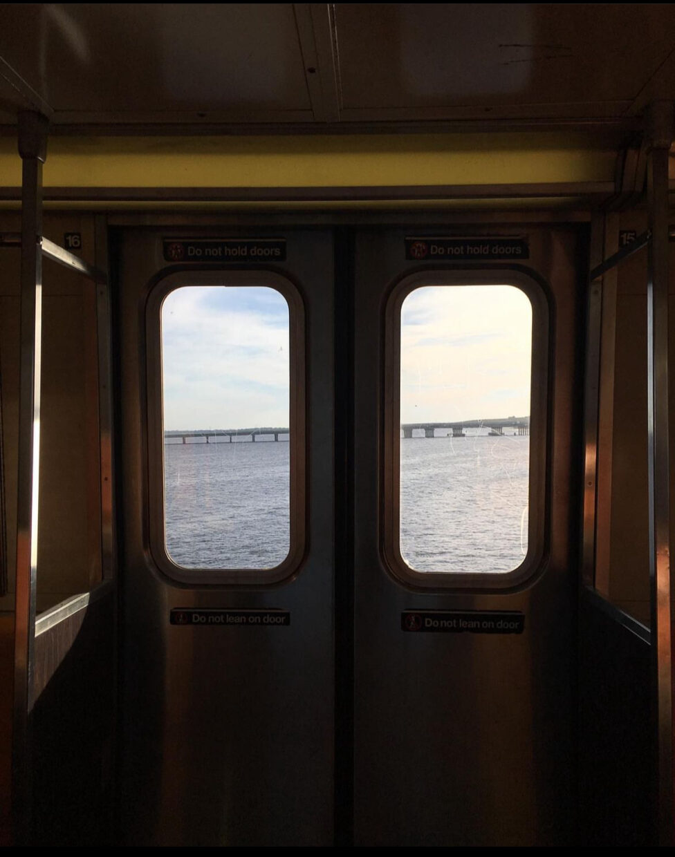 [Two subway doors overlook a bridge above a body of water during golden hour.]