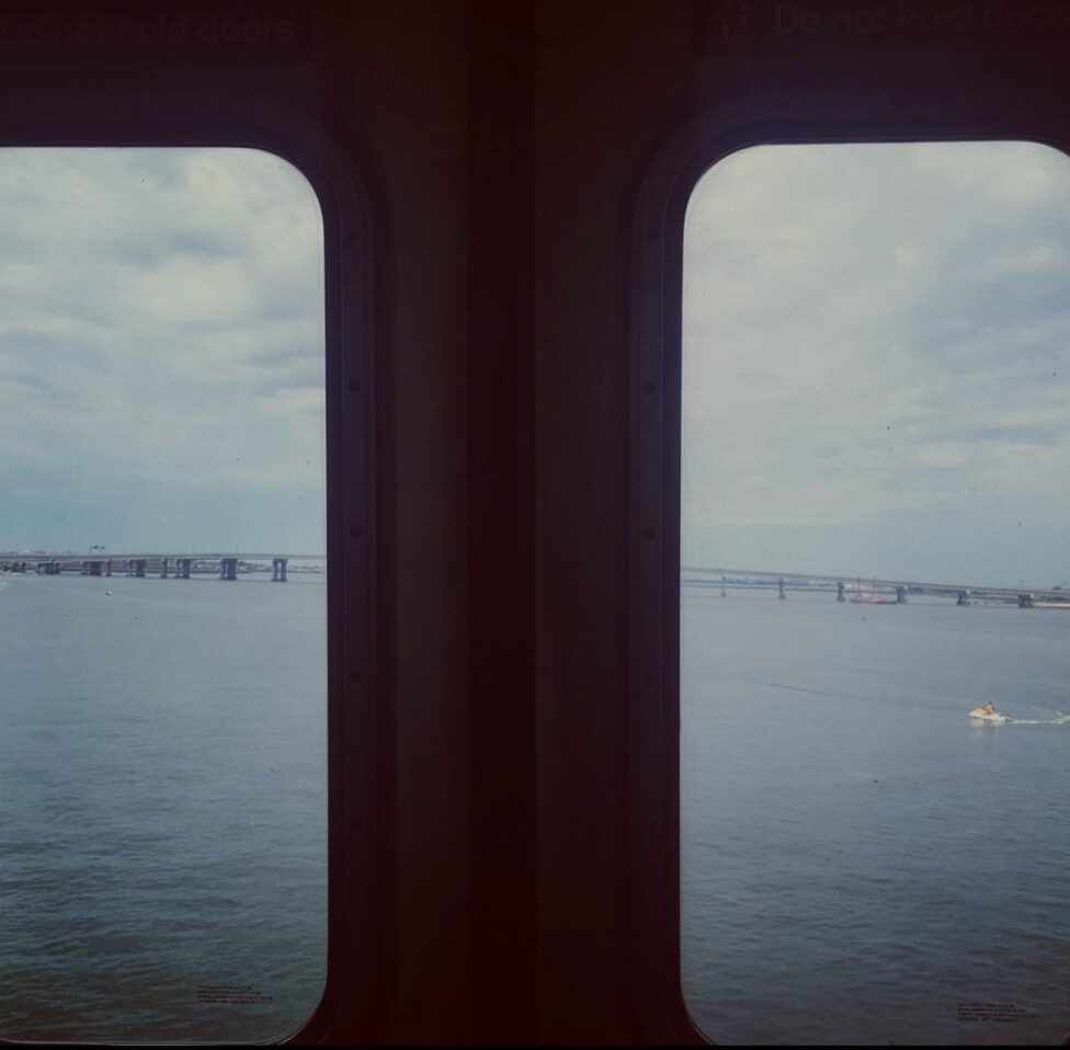 [Encuadre de puertas plateadas y dos ventanas por las que se ve un puente sobre el mar y una persona encima de un 
