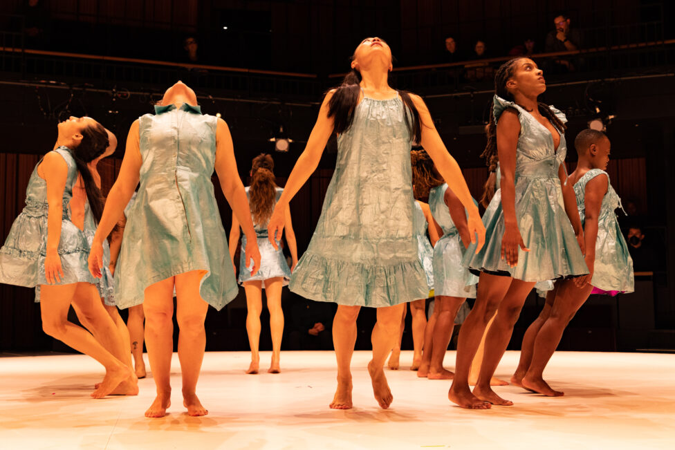 Dancers Isabel Umali, Natalie Green, Jin Ju Song-Begin, Brooke Ashley, and Mawu Ama Ma’at Gora wear pale blue knee-length dresses as they stand in a circle, tilting their heads back and chests toward the sky. Photo courtesy of the artists. 