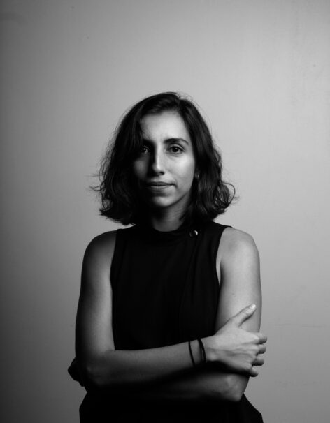 Black and white portrait of Lori Kharpoutlian. She has straight shoulder-length hair and a black top. She looks into the camera with a subtle smile. Her arms are crossed in front of her. Photo by Dimitri Haddad.
