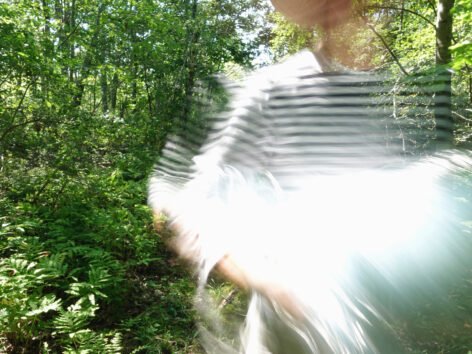 Woman in a striped shirt carrying light through the forest.