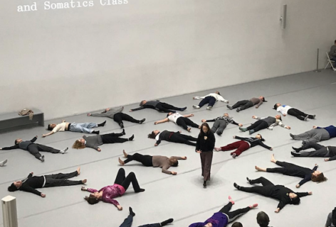 Photo of Shelly Senter teaching at MoMA. She stands in the center while the student lay on their back in star position. Photo courtesy of the artists.
