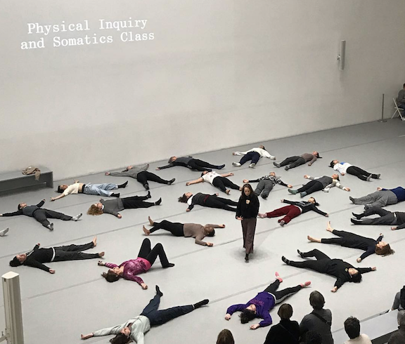 Photo of Shelly Senter teaching at MoMA. She stands in the center while the student lay on their back in star position. Photo courtesy of the artists.