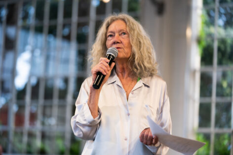 Sara Shelton Mann wears a white shirt and speaks in to a microphone. Photo by Robbie Sweeney.