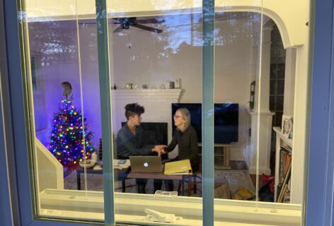 Guest editor Leah Wilks and Annie Dwyer are photographed planning Experiential Anatomy Workshop from the outside of a barred window. Photo credit to Em Pike.
