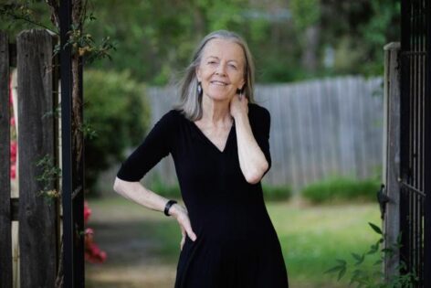 Annie, a white woman wearing a black dress, posing at the opening of the wooden gate in an outdoor setting. 