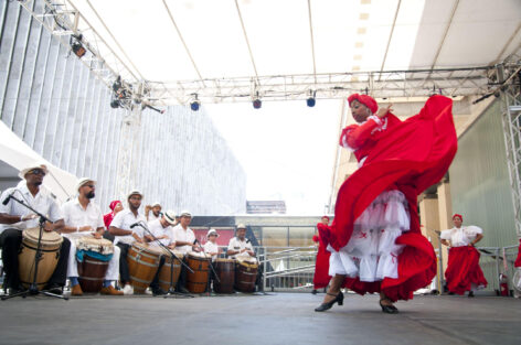 Bomba dancer wearing a black top , red skirt and white pants dancing to the drummer who has his bomba drum, white top and black pants. photo courtesy of artist