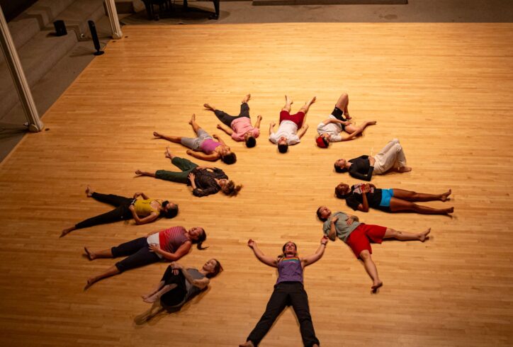 Dancers lay down on the hardwood floor at Judson Memorial Church with their heads facing toward the center. 2024 Summer MELT with Vicky Schick. Photo by Rachel Keane.