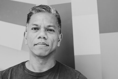 A brown-skinned Filipino man with graying hair looks directly into the camera against a geometric-patterned wall. Photo by Katherine Helen Fisher.