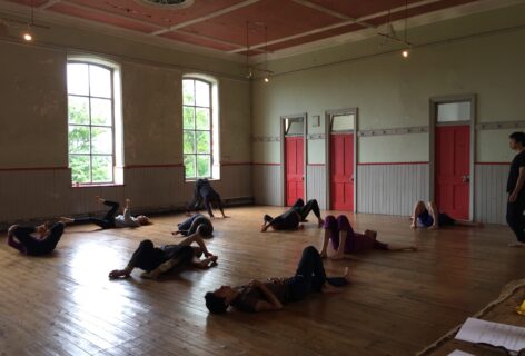 A photo of dancers spread out on a wood floor studio. They lay on their backs with their feet propped up. Photo by K.J. Holmes.