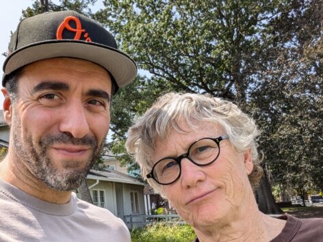 Image of person with a hat on the left and a smaller person to the right with black glasses and short hair. Photo by Serouj Aprahamian.