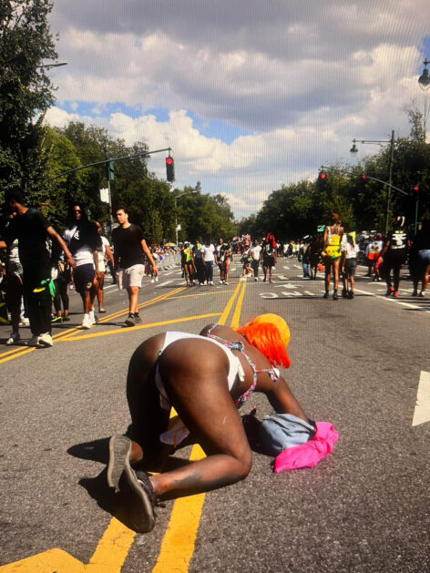 ASS UP ON EASTERN PARKWAY LABOR DAY 9/1/2024 CARRIBEAN DAY PARADE. Crackheadbarney on hand and knees in the middle oft the street. She wears a bright orange wig and white shorts. Photo courtesy of the artist.