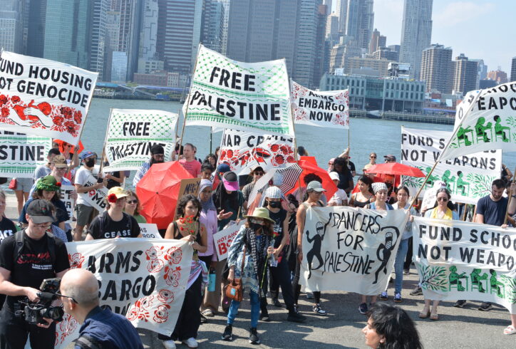 At a Not Another Bomb rally in front of the Hudson River, protesters close their eyes for a moment of silence, holding signs reading 