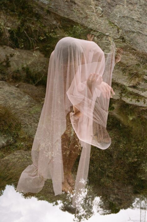 A layering of multiple exposed images of Juliet draped in a pink fabric outlining her shifting silhouette, with fragmented hands and feet peeking out. The background is the layered images of the high-altitude, mountainous region of La Calera, Colombia. Photo by Daniela Flo