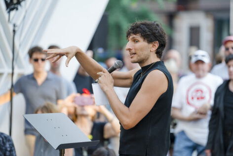 Morgan Bassichis performs at NYCAM. They are in a black tank top and hold a microphone to their mouth. Photo courtesy of artist.