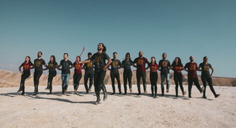 Dabke performance by El-Funoun Dance Troupe in the hills of Jericho, Palestine. Line up of Dabke dancers with the Laweeh/ leader in front, dressed in jeans and El-Funoun T-Shirt and Dabke boots. Photo courtesy of the artists.