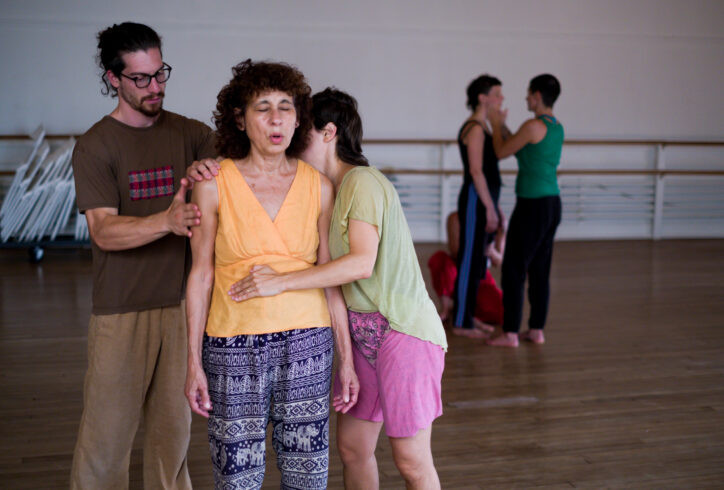 Two people providing touch and physical support to a workshop participant whose eyes are closed and mouth is open, making sound. Photo by Anna M. Maynard.