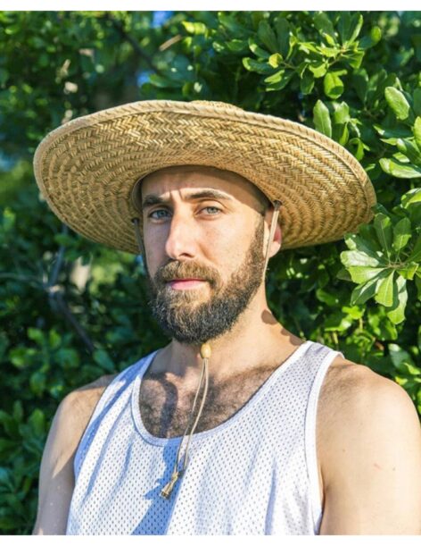 Burr Johnson looks into the camera with a neutral expression. He wears a white tank top and a straw hat. Photo courtesy of the artist.