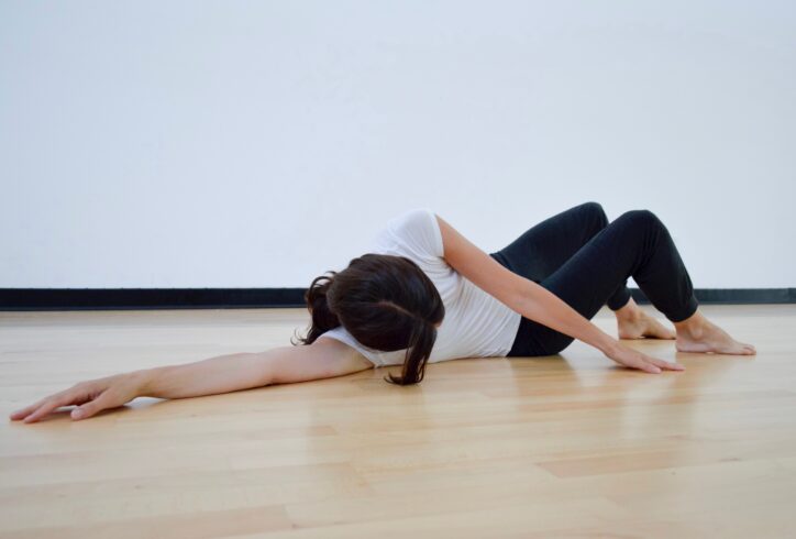 A bright studio. A dancer lays on the floor legs bet and arm reaching behind them. Photo by Rauschenberg Foundation