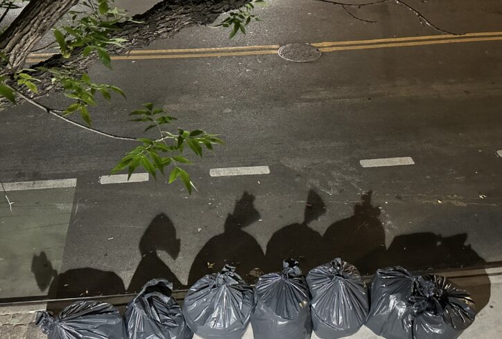 A photo of black trash bags on a sidewalk. They are lit by a street lamp. Photo courtesy the artist.