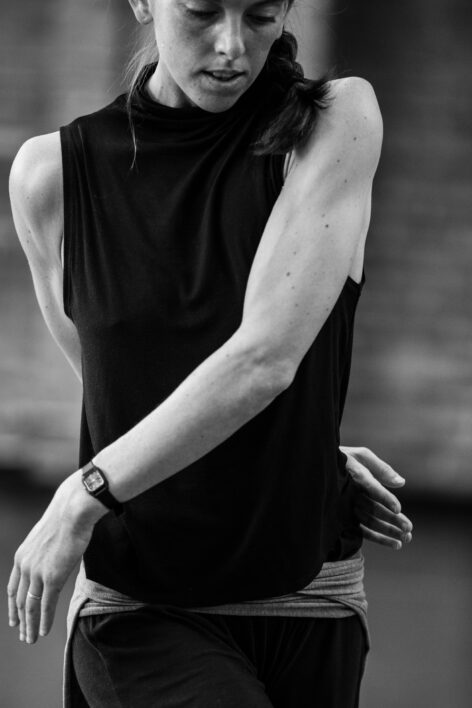 Black and white image of a dancer moving her arms across her body. 