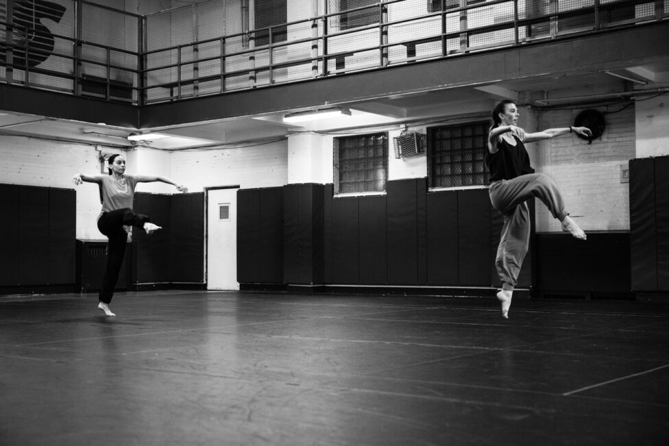 A black and white photo of two figures engaged in a dynamic jump. Photo credit to Maria Baranova.