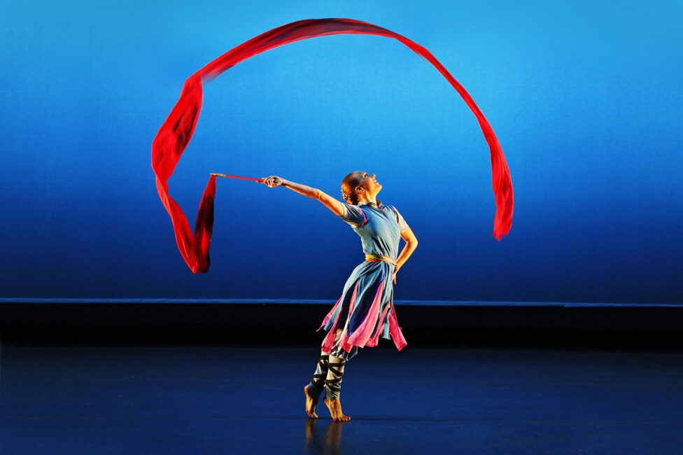 A vibrant red ribbon cascades over a beaming dancer. Photo credit to Paul Goode.