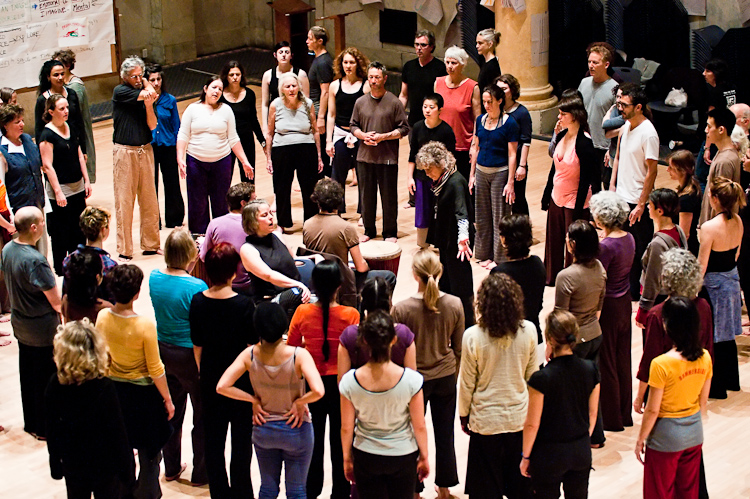 From the MR Archives, 2010. Photo by Ian Douglas. People gather around Anna Halprin in a circle inside an open indoor church.