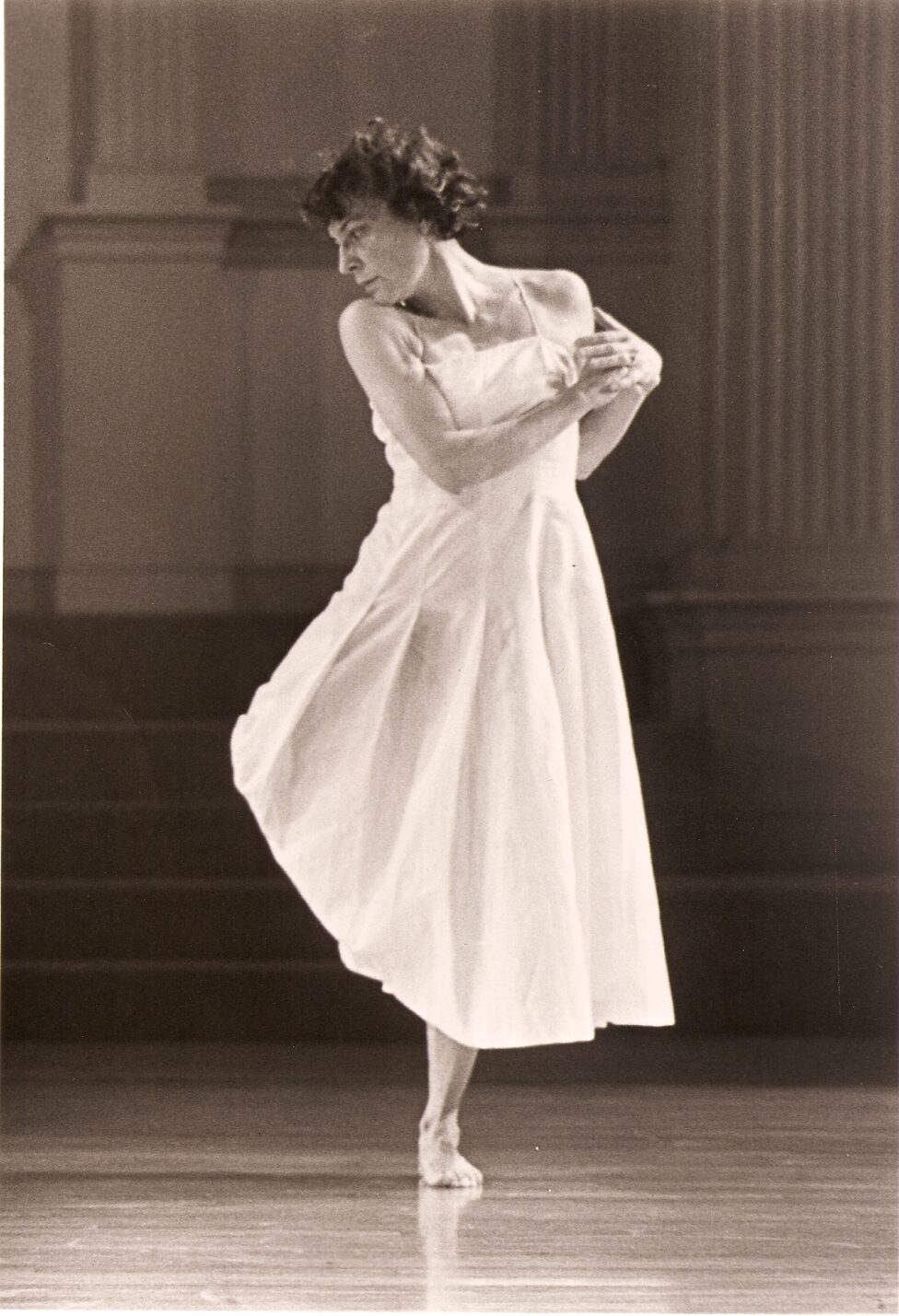 From the MR Archives, 2000. 9th IFNY photo by Tom Brazil. Mary Overlie, in a white dress balances on one leg with her gaze and chin towards her right shoulder.