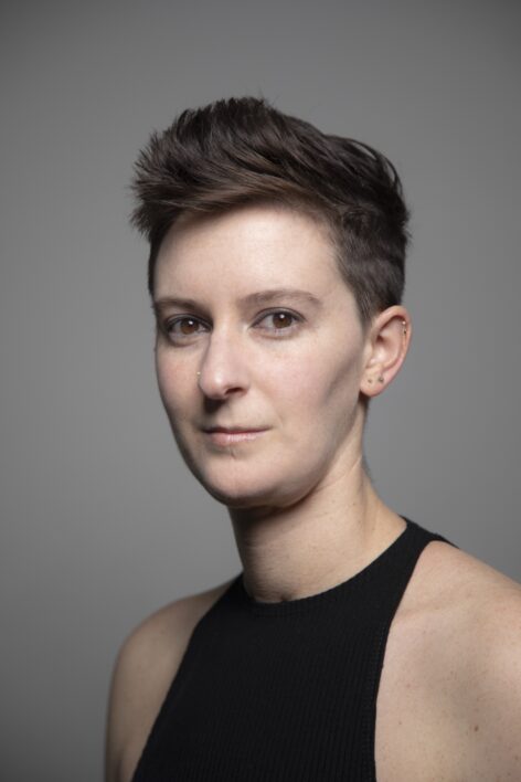 Nadia Hannan, a white person with short brown hair and brown eyes, looks directly at the camera in front of a gray background. Photo by Blaga Ditrow