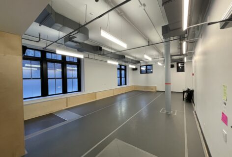 A dance studio with grey marley floor and one grey column towards one end of the room.