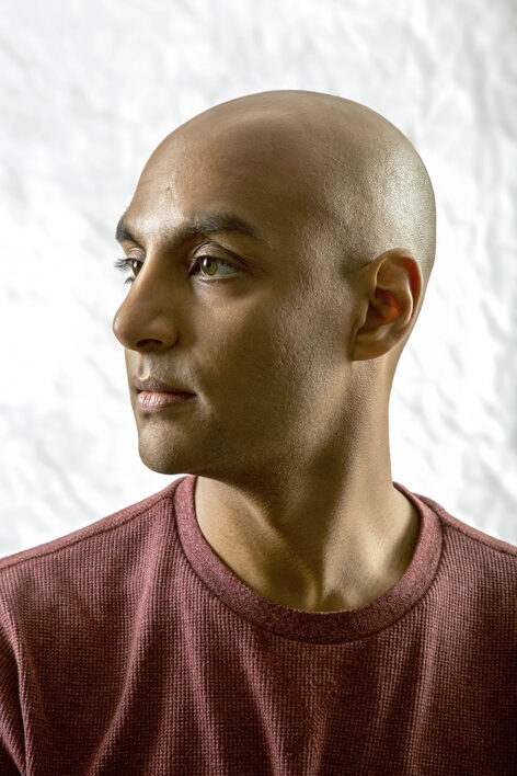 A close up visual of the left side of Paul's face. On display are his brown eyes, brown skin, shaved head, while he wears a burgundy warm shirt. Photo by Andrew Jordan